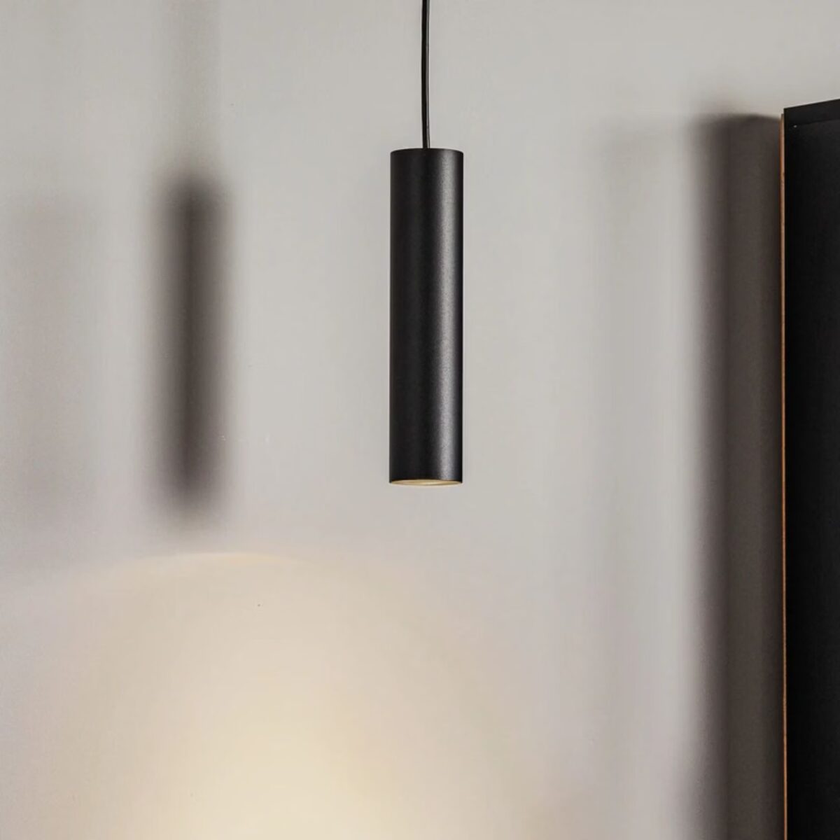 Einzelne schwarze Röhrenpendelleuchte, deren Schatten auf die Wand fällt
