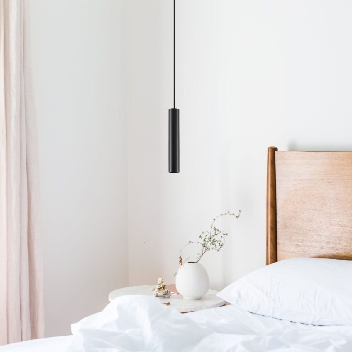 Schmale schwarze Röhrenpendelleuchte über einem Nachttisch neben einem Holzbett