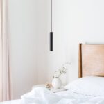 Schmale schwarze Röhrenpendelleuchte über einem Nachttisch neben einem Holzbett