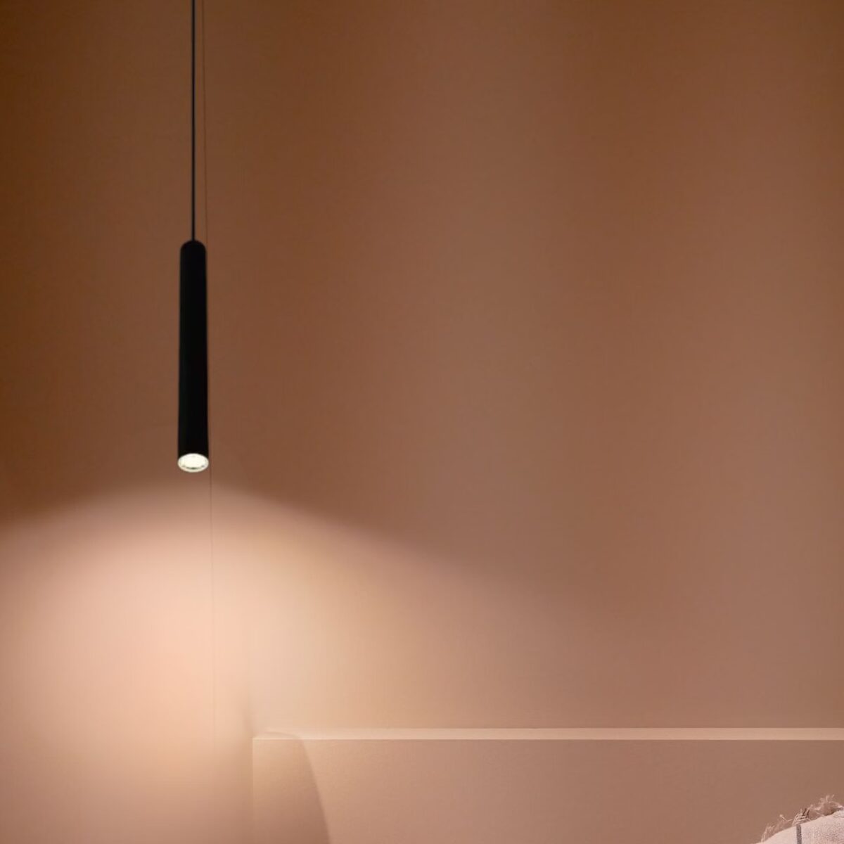 Schwarze Röhrenpendelleuchte, die einen warmen Lichtkegel auf eine braune Wand wirft