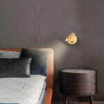 Einstellbare, goldfarbene Wandleuchte aus Messing neben einem Bett über einem Nachttisch