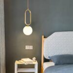 Goldene Hängeleuchte aus Glasstein in modernem Design auf grauem Hintergrund mit einem Bett auf der rechten Seite