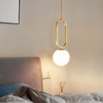 Goldene Ring-Pendelleuchte mit runder Opalglaskugel, eingeschaltet über einem Nachttisch
