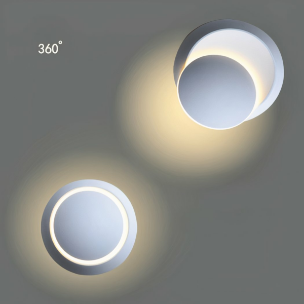 Weiße, runde Wandleuchte, die an einer dunkelgrauen Wand eingeschaltet ist. In der Mitte befindet sich eine Art rundes Plättchen, das um 360° gedreht werden kann.