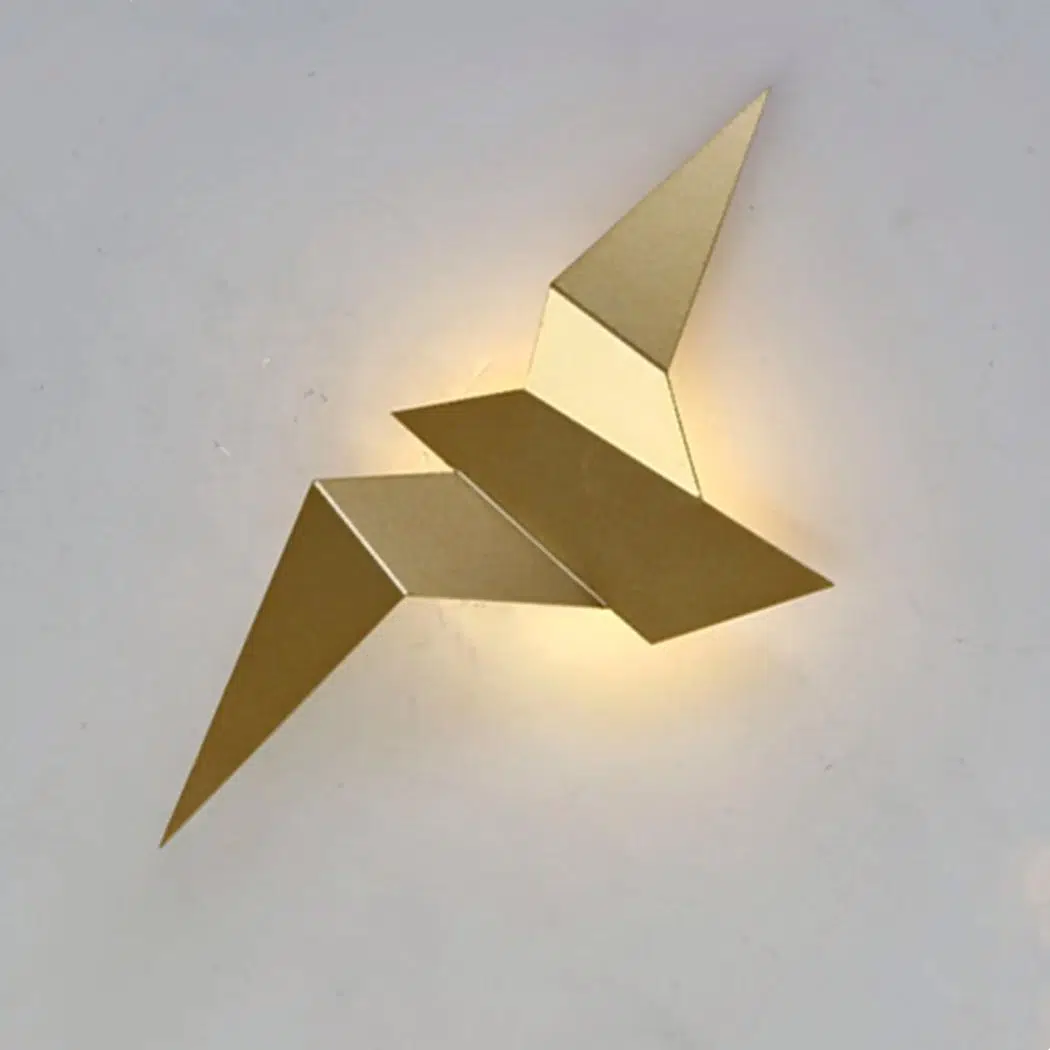LED-Wandleuchte in Form eines fliegenden Vogels mit Origami-Effekt Auf einem weißen Hintergrund sehen Sie eine goldene Wandleuchte in Form eines Vogels im Origami-Stil.