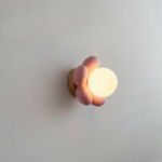 Sur un fond blanc on voit une applique murale en forme de fleur rose allumée.