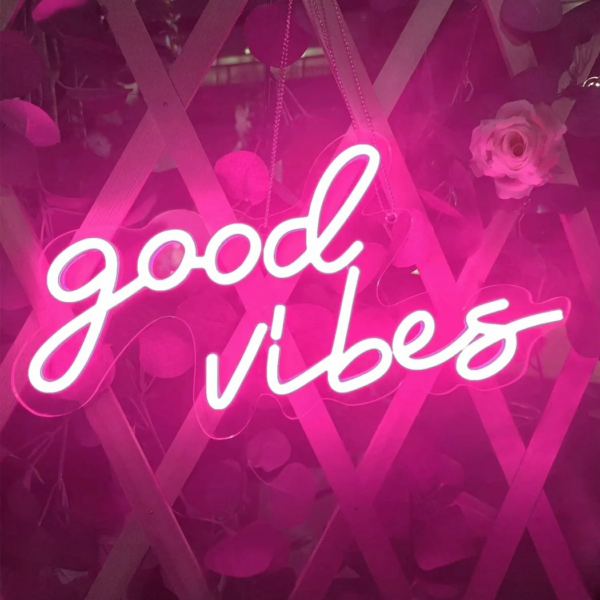 Sie sehen eine neonpinkfarbene Wandleuchte mit dem Schriftzug good vibes, die eingeschaltet ist.