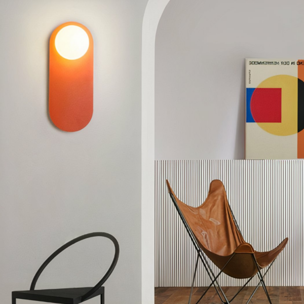 Orangefarbene Designer-Wandleuchte, in einem schlichten Raum neben einem Künstlerbild und einem Stuhl