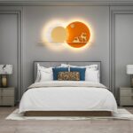 Orangefarbene Wandleuchte mit zwei Hirschen in zwei Kreisen, die wie zwei übereinander liegende Sonnen aussehen, über einem Bett