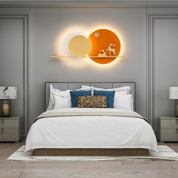 Orangefarbene Wandleuchte mit zwei Hirschen in zwei Kreisen, die wie zwei übereinander liegende Sonnen aussehen, über einem Bett