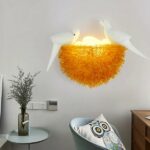In der Mitte des Bildes sehen Sie eine Wandapplikation in Form eines Vogelnestes. In der unteren linken Ecke des Bildes sehen Sie einen Tisch mit einer grau-transparenten Vase mit Zweigen darin. In der rechten unteren Ecke sehen Sie einen Sessel mit einem Kissen mit Eulenmotiv.