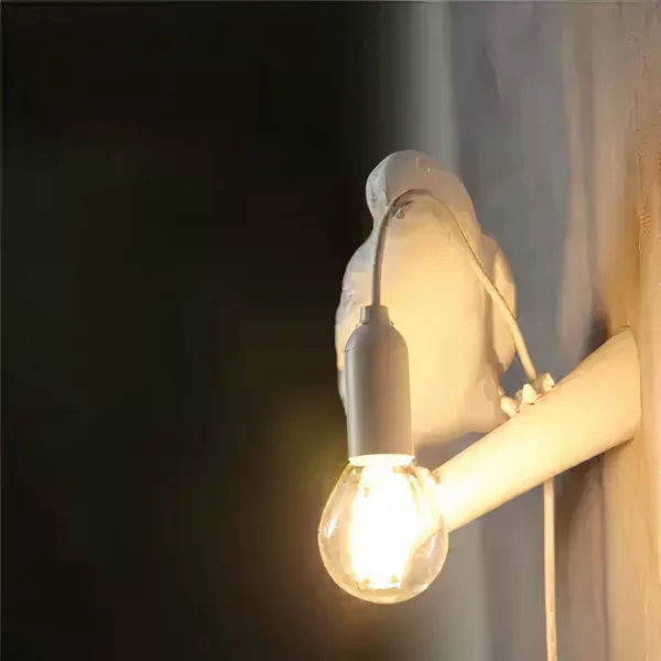 Auf einem schwarzen Hintergrund sehen Sie eine eingeschaltete weiße Wandleuchte in Form eines Raben.