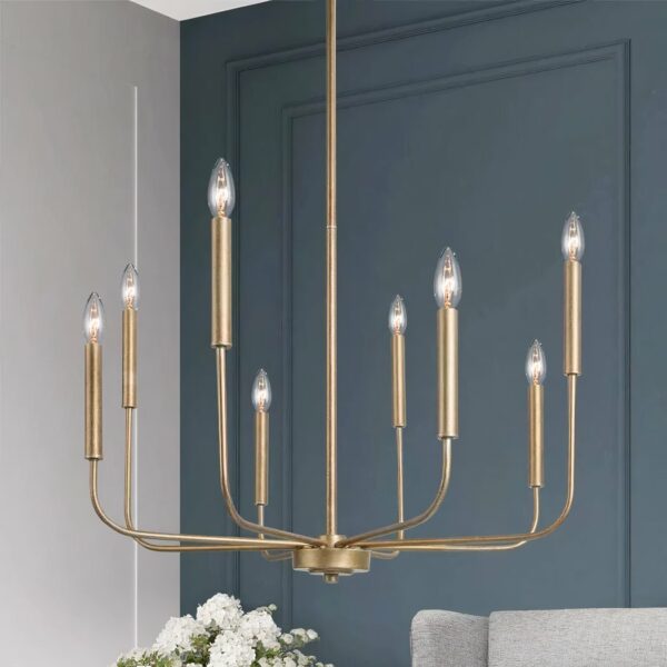 Kronleuchter en métal doré, en forme de chandelier avec 8 bougies à ampoule. Derrière, au fond, on voit un mur bleu canard, un bout de bouquet de fleurs blanches et un bout de canapé gris clair.