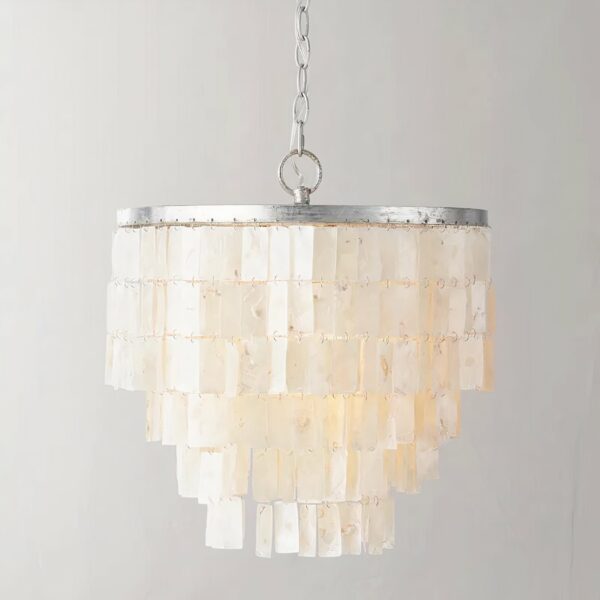 Suspension en nacre suspendue par une chaine argentée. Composé d'une armature ronde argenté orné de perles de nacre plates et rectangulaires qui forme une grappe. Sur un fond gris.