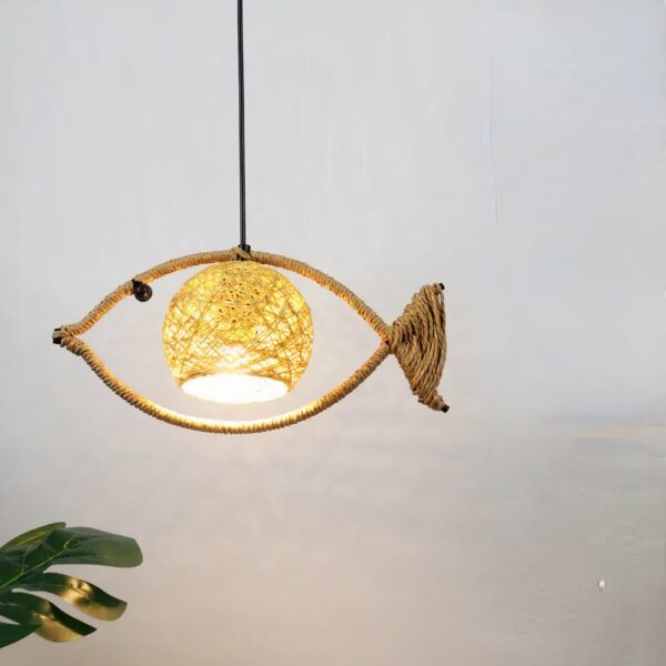 Kronleuchter en corde enroulée autour d'une tige métallique en forme de poisson, suspendu. Avec une abat-jour au centre en forme de boule. Derrière on voit un mur gris et en bas à gauche on voit un morceau de plante verte.