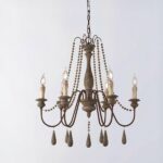 Kronleuchter en laiton et bois avec 6 chandelles, les ampoules remplacent la flemme des bougies. Décorées de perles, des allongées qui se trouvent sous chaque chandelle et des plus petites sur le reste du lustre. Sur un fond gris.