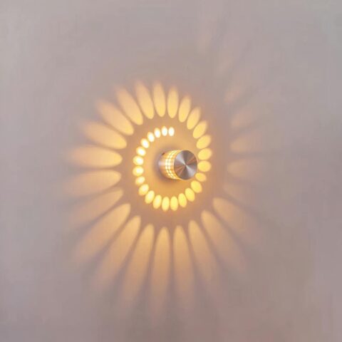 Runde LED-Wandleuchte aus silbernem Aluminium, eingeschaltet, projiziert eine Spirale aus warmem Licht auf eine weiße Wand