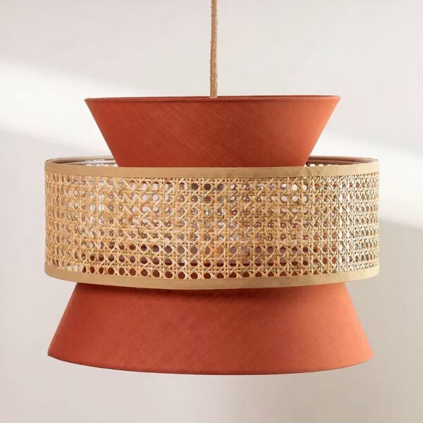 Kronleuchter terracotta et beige, suspendu par un câble au centre. Composé d'un abat-jour en tissu couleur terracotta en forme de sablier, et d'un cercle en cannage qui entoure le sablier au centre. Sur un fond gris très clair.