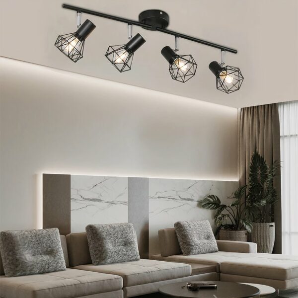 Schwarzer Deckenkronleuchter im Industriestil mit 4 Glühbirnen im Stil von Industriespots in einer Reihe. In einem Wohnzimmer mit einem großen beigen Ecksofa mit 3 rechteckigen Kissen. Eine grüne Pflanze in der rechten Ecke des Sofas und ein brauner Vorhang dahinter.