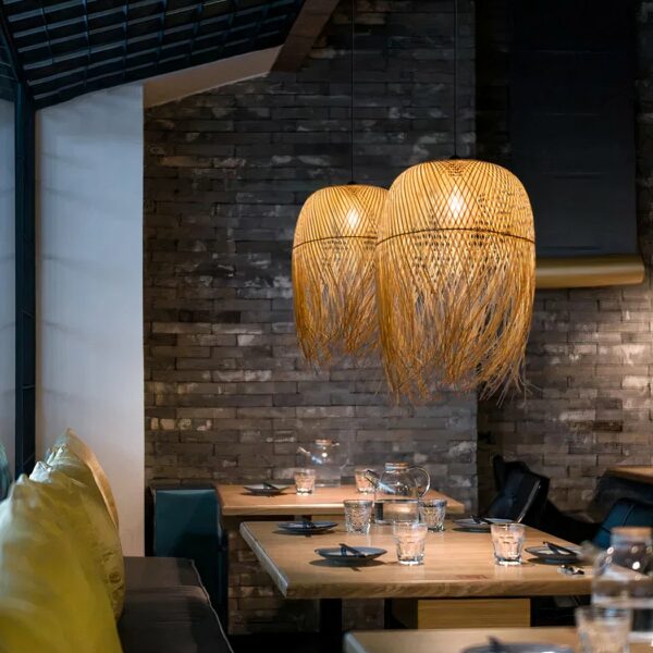 Traditioneller handgewebter Kronleuchter aus Stroh, der über Esstische in einer Umgebung, die wie ein Restaurant aussieht, aufgehängt und beleuchtet wird.