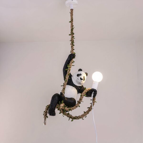 Hängeleuchte mit einem Hanfseil, das mit Blättern umwickelt ist. Ein Panda hängt an seiner rechten Vorderpfote, das Seil läuft durch seine Hinterpfoten und er hält eine brennende Glühbirne in seiner linken Vorderpfote mit einem Teil des Seils.