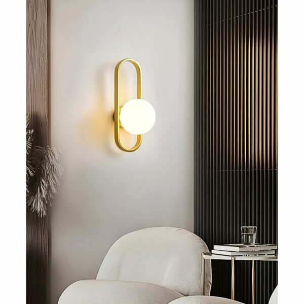 sie sehen in Ihrem Wohnzimmer mit einem weißen Sessel eine moderne goldene Wandleuchte mit einer Kugel