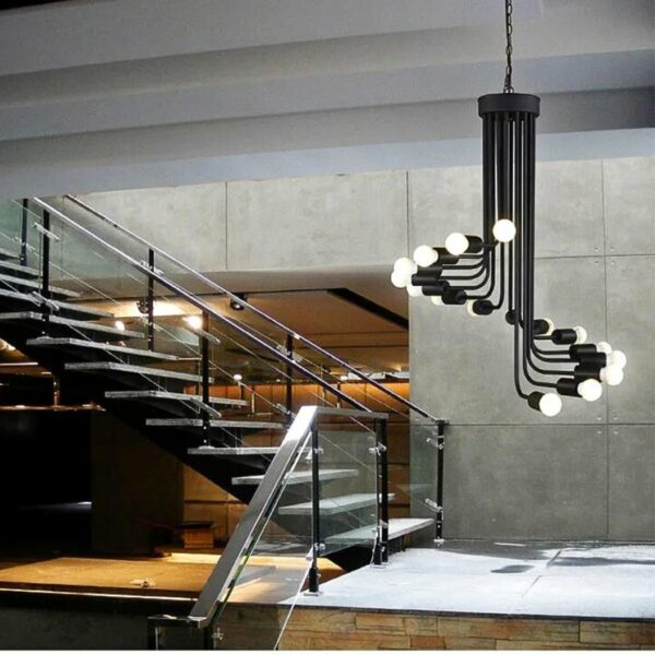 sie sehen in einem Wohnzimmer mit einer Treppe im Hintergrund einen schwarzen schmiedeeisernen Kronleuchter mit sichtbaren Glühbirnen