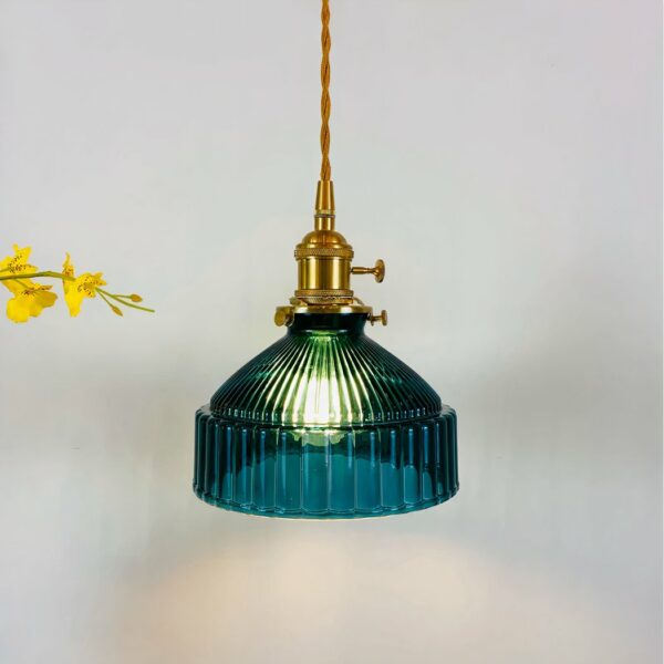Vintage-Hängeleuchte mit goldfarbenem, gedrehtem Kabel und goldfarbener Lampenfassung. Der duckblaue Lampenschirm sieht aus wie eine Glocke mit umlaufenden Rillen. Die Glühbirne ist eingeschaltet. Gelbe Blumen auf der linken Seite.