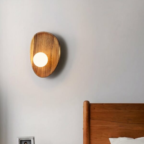 Wandleuchte aus Holz im Muschelstil mit einer kleinen Leuchtperle, die an der Wand eines Schlafzimmers neben dem Bett aufgehängt wird.
