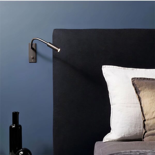 Wandleuchte mit Leseleuchte und Schalter, die an einer blauen Wand in einem Schlafzimmer neben einem Bett hängt.