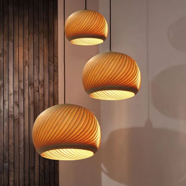 3 suspensions similaires en bois nervuré forme ronde, suspendue à différentes hauteurs, diffusant une lumière chaude.
