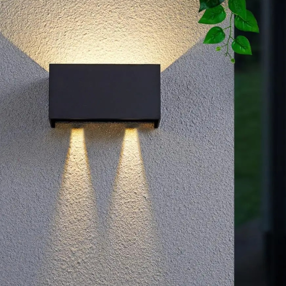 Schwarze rechteckige LED-Außenwandleuchte mit Lichtschein nach oben und unten neben Blättern